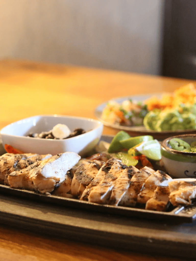 Grilled chicken with lime, salsa, and side dishes on a serving platter.