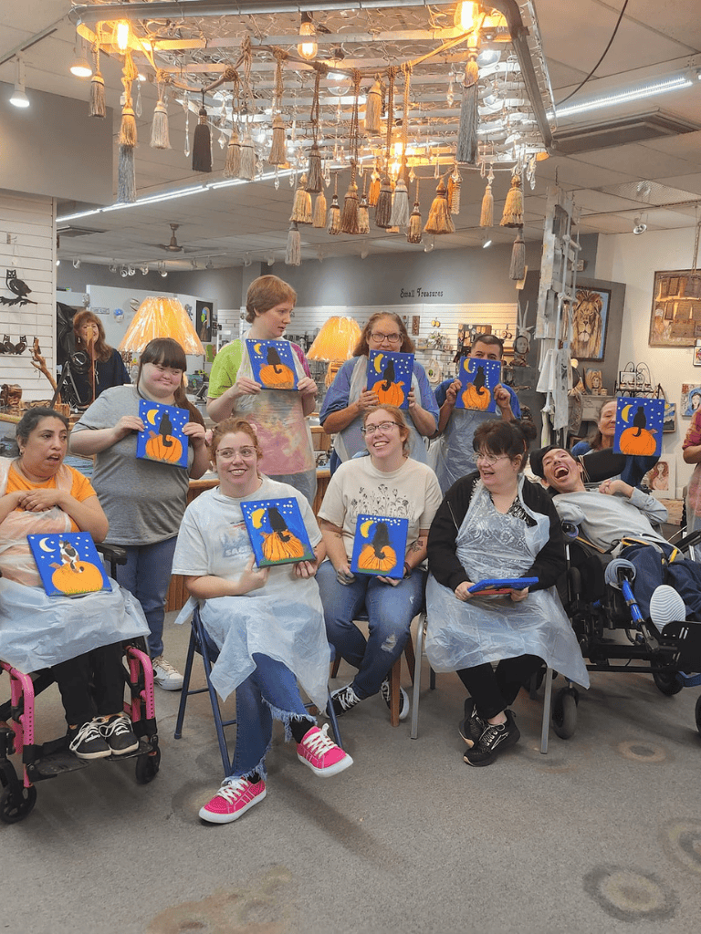 Colorful group of children and adults displaying Halloween-themed artwork at QuestForDirections art workshop.