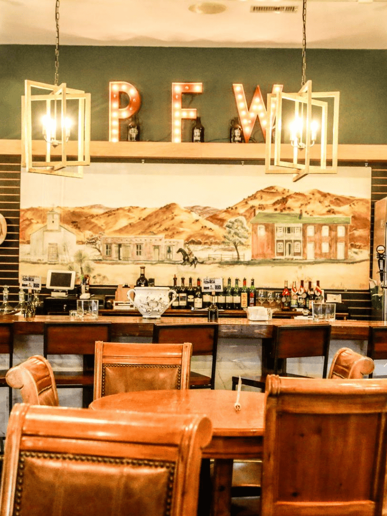 Cozy restaurant interior with rustic wooden furniture and warm ambient lighting, featuring bar area and artwork.