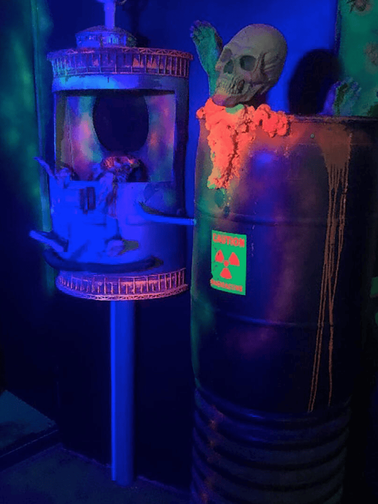 Skull and radioactive waste barrel exhibit in a dimly lit, neon-blue themed escape room scene.
