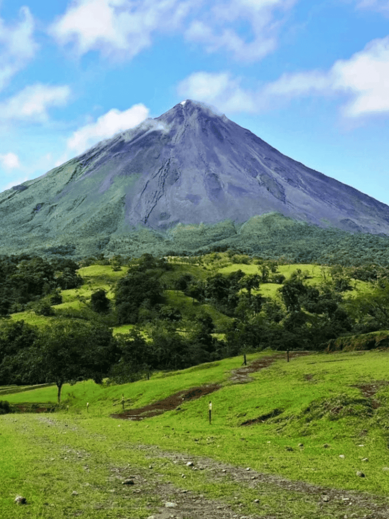 Volcano surrounded by lush green landscape and bright blue sky with clouds.