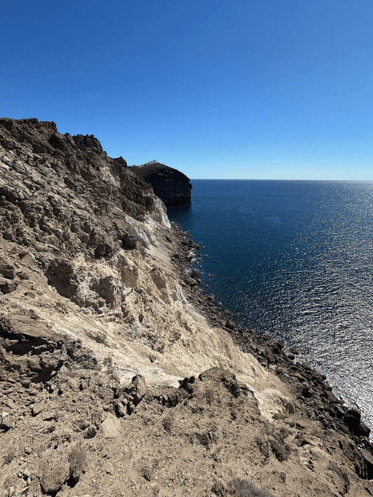 Vast rocky coastal cliff overlooking the ocean beneath a clear blue sky.