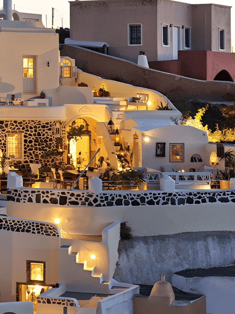 Vibrant Santorini village with whitewashed buildings, terraces, and warm evening lights.