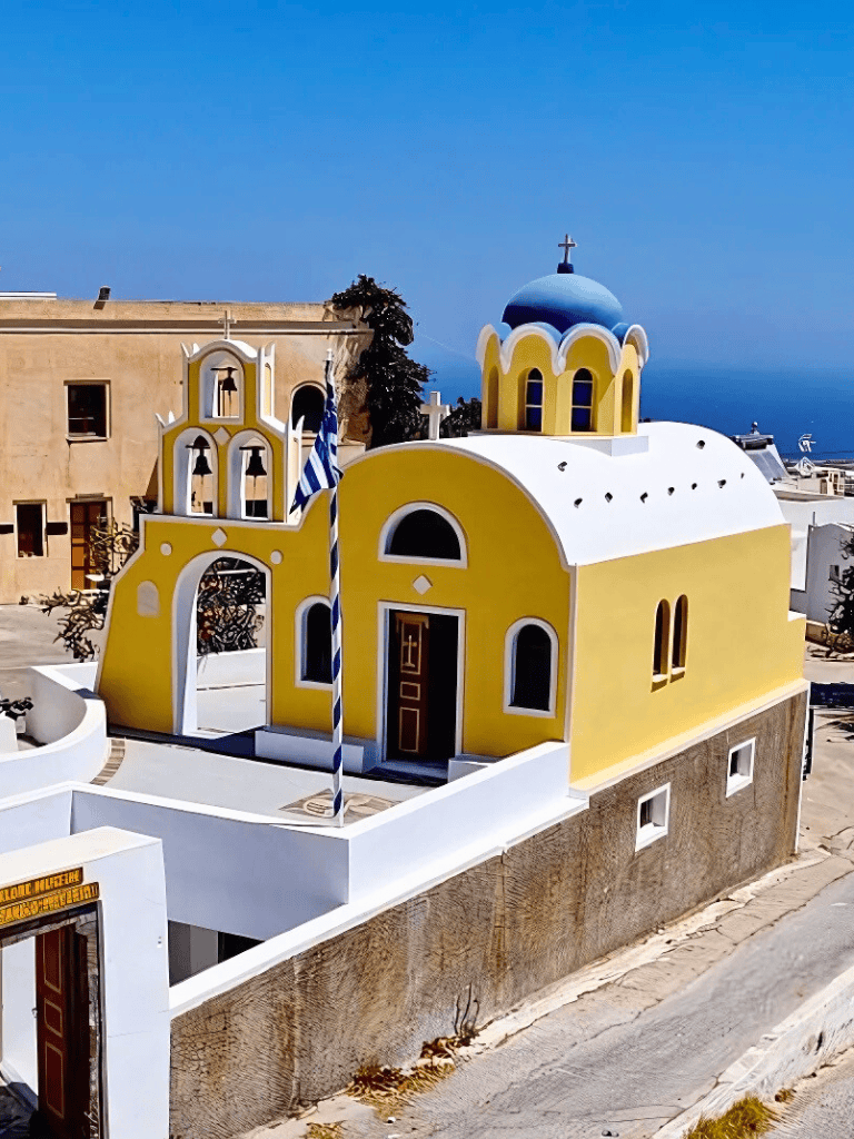 Colorful Greek Orthodox church in Santorini, Greece with distinctive blue dome and vibrant yellow walls.