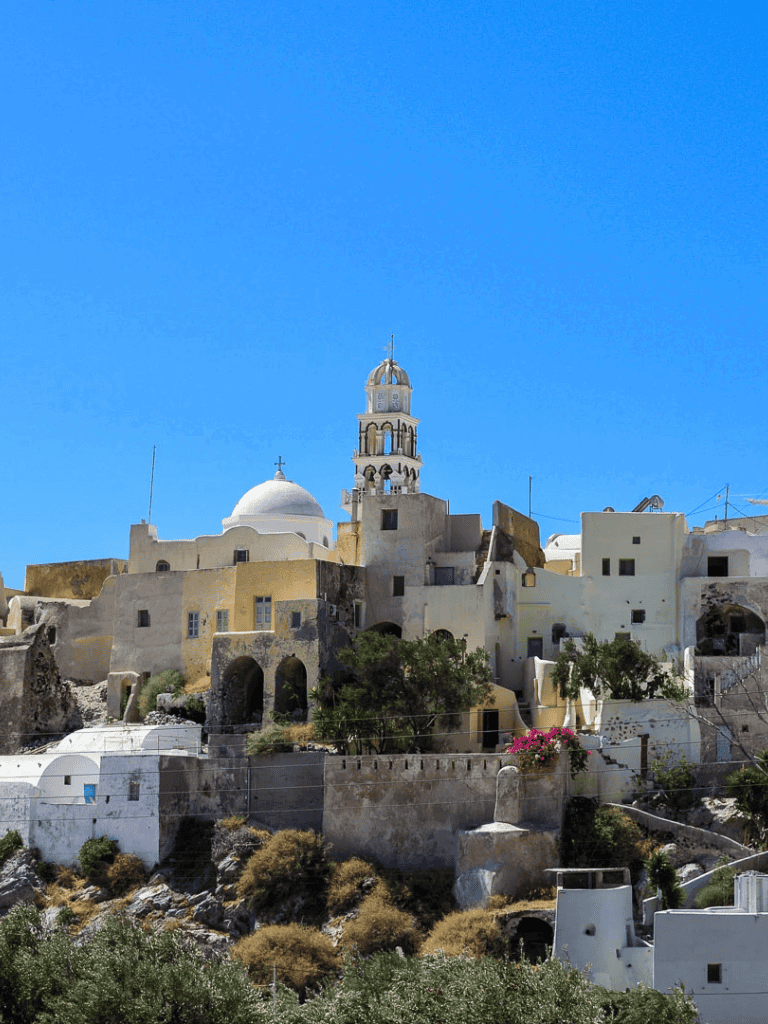 Colorful hillside village with white buildings and a prominent bell tower in Greece.