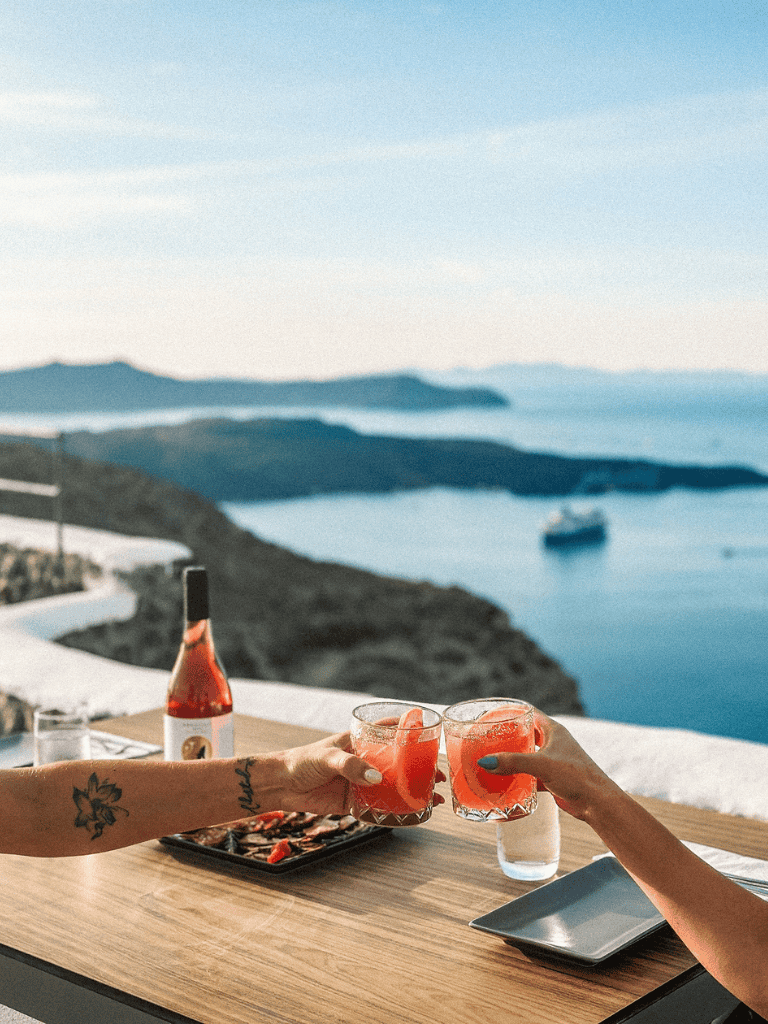 View of a seaside terrace with two people raising drinks, overlooking Greek islands, destination travel, and scenic views.
