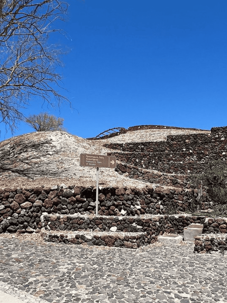 Ancient ruins with stone steps and a directional sign at archaeological site in Arad, Greece.