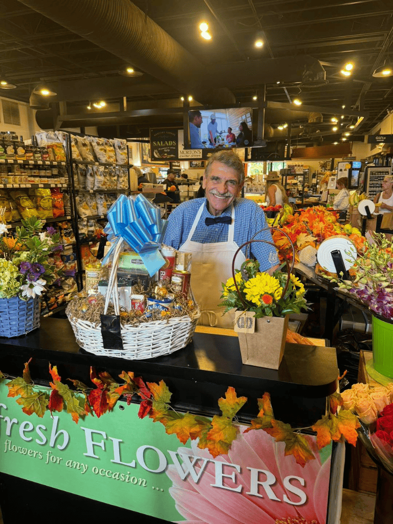 Joyful man at flower shop register with colorful blooms and gift baskets, celebrating special occasions.
