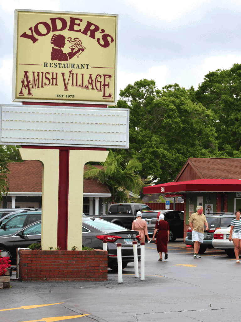 Yoder’s Amish Village restaurant and store sign, parking lot with visitors, in a rural setting.