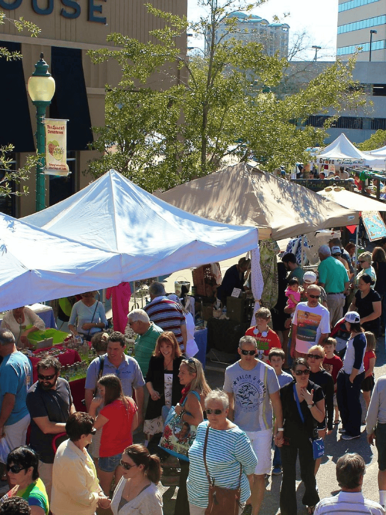 Vibrant downtown street market bustling with diverse shoppers and colorful tents on sunny day.