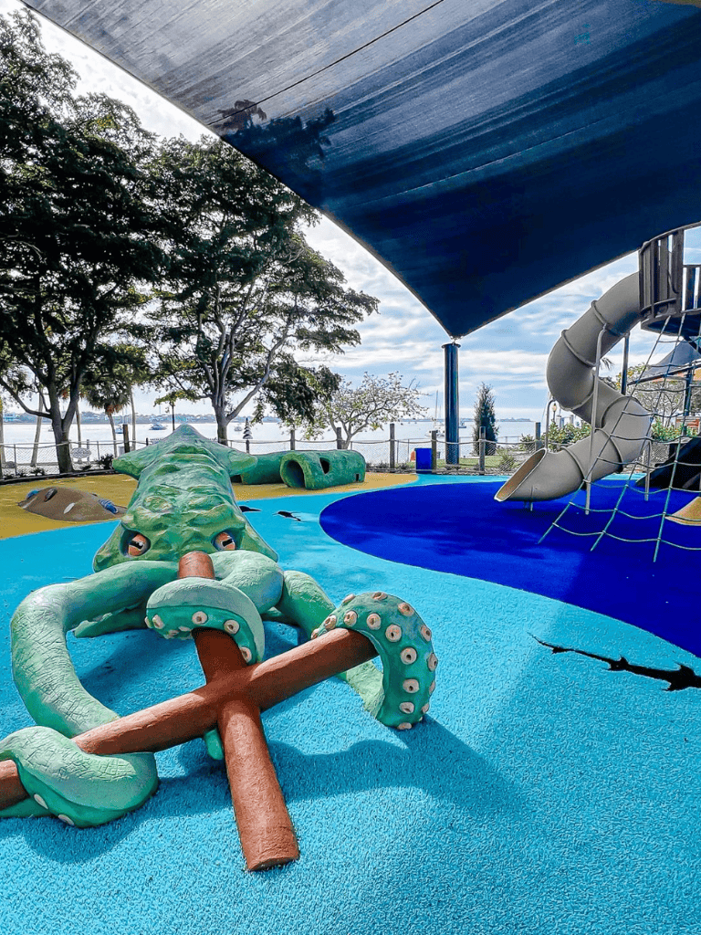 Colorful aquatic-themed children's splash park with slides and play structures by a waterfront.