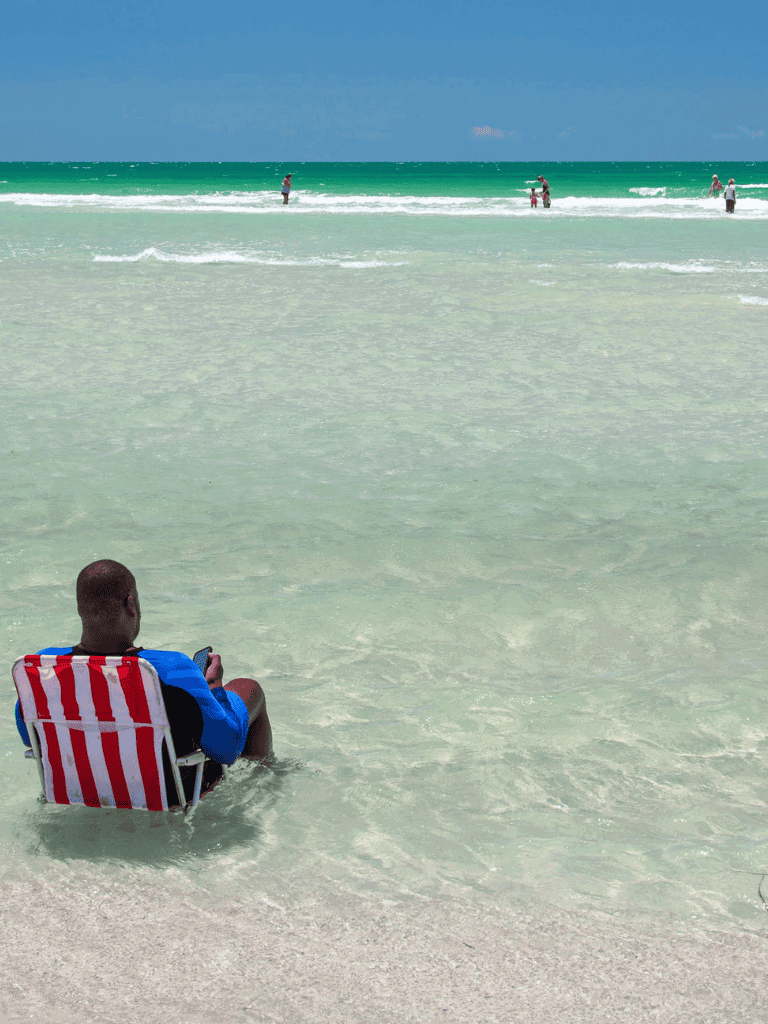 Relaxing beach scene with man sitting on a striped chair in shallow water.
