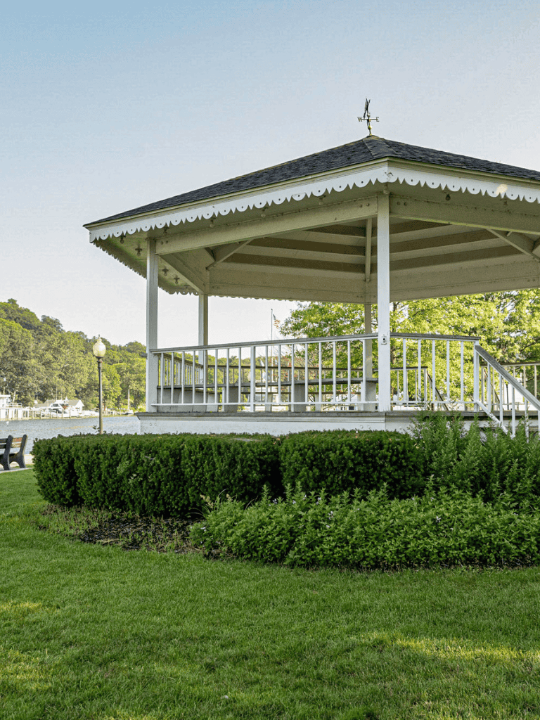 Cozy park pavilion overlooking a scenic waterfront with lush greenery and a well-maintained lawn.