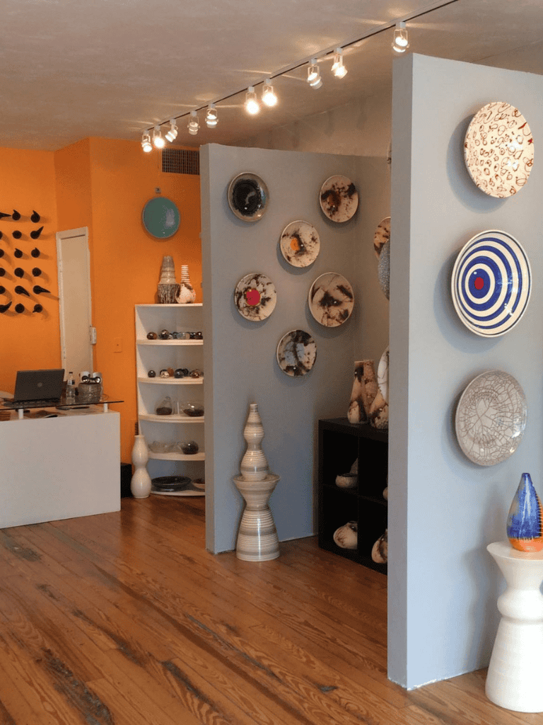Smooth indoor space with decorative pottery, shelves, and vibrant orange and blue walls, showcasing art and design.