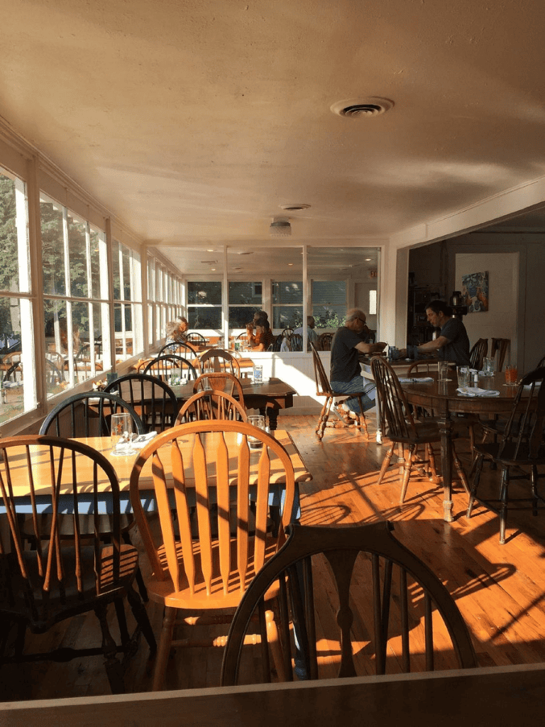 Warm sunlight inside cozy restaurant with wooden chairs and tables, inviting atmosphere for dining.