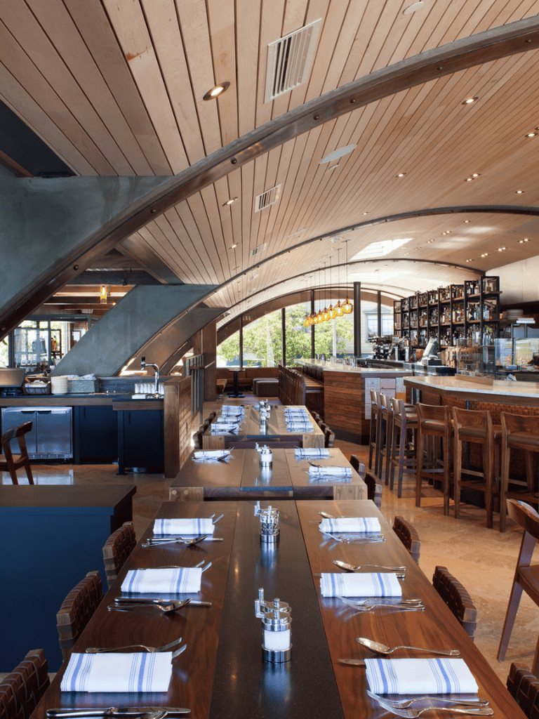 Elegant restaurant interior with wooden accents, modern lighting, and organized table settings for dining.