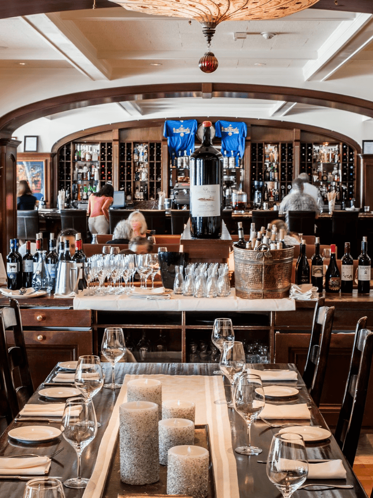 Elegant restaurant bar with wine bottles, glassware, and a cozy dining table setting for a sophisticated dining experience.