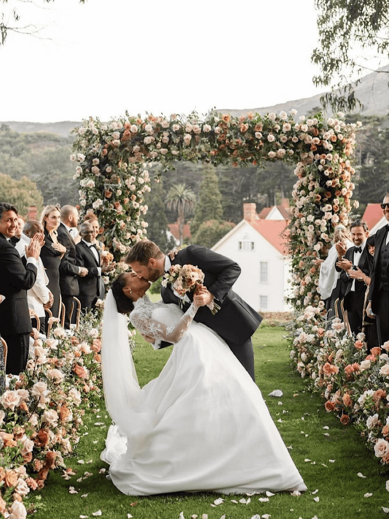 Elegant outdoor wedding ceremony with floral arch and lush garden setting, capturing romantic bride and groom moments.