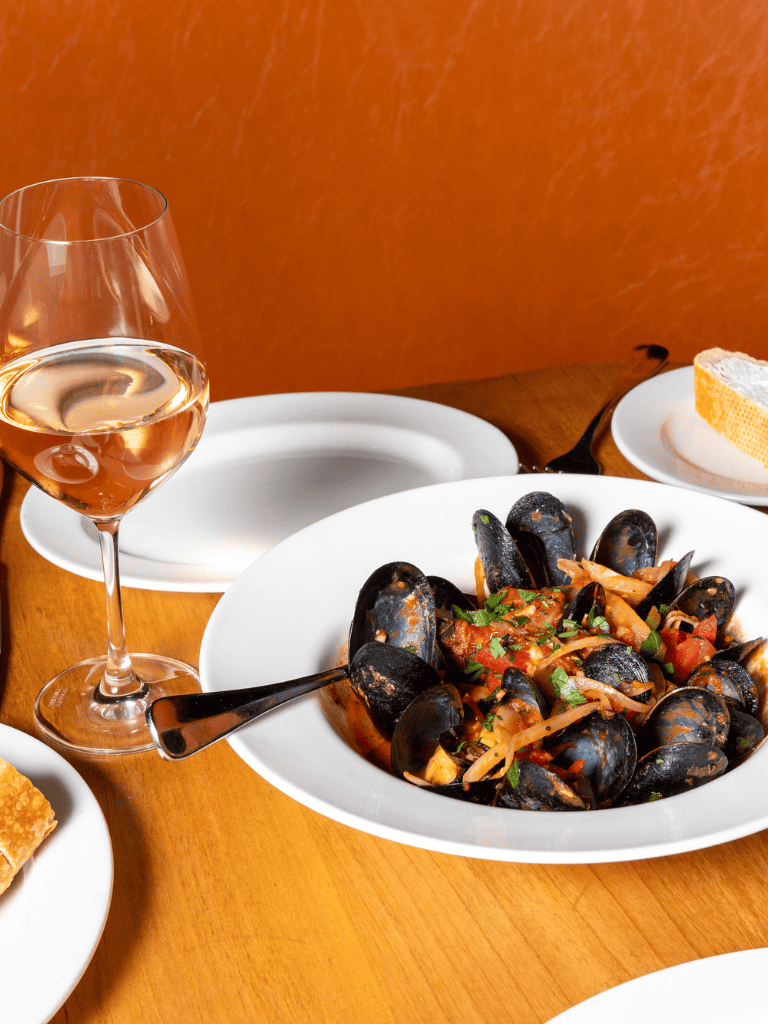 Delicious mussels in tomato sauce with herbs, served with a glass of rosé wine on a wooden table.