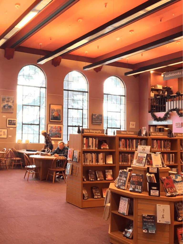Comfortable bookstore interior with large windows, bookshelves, and customers browsing.