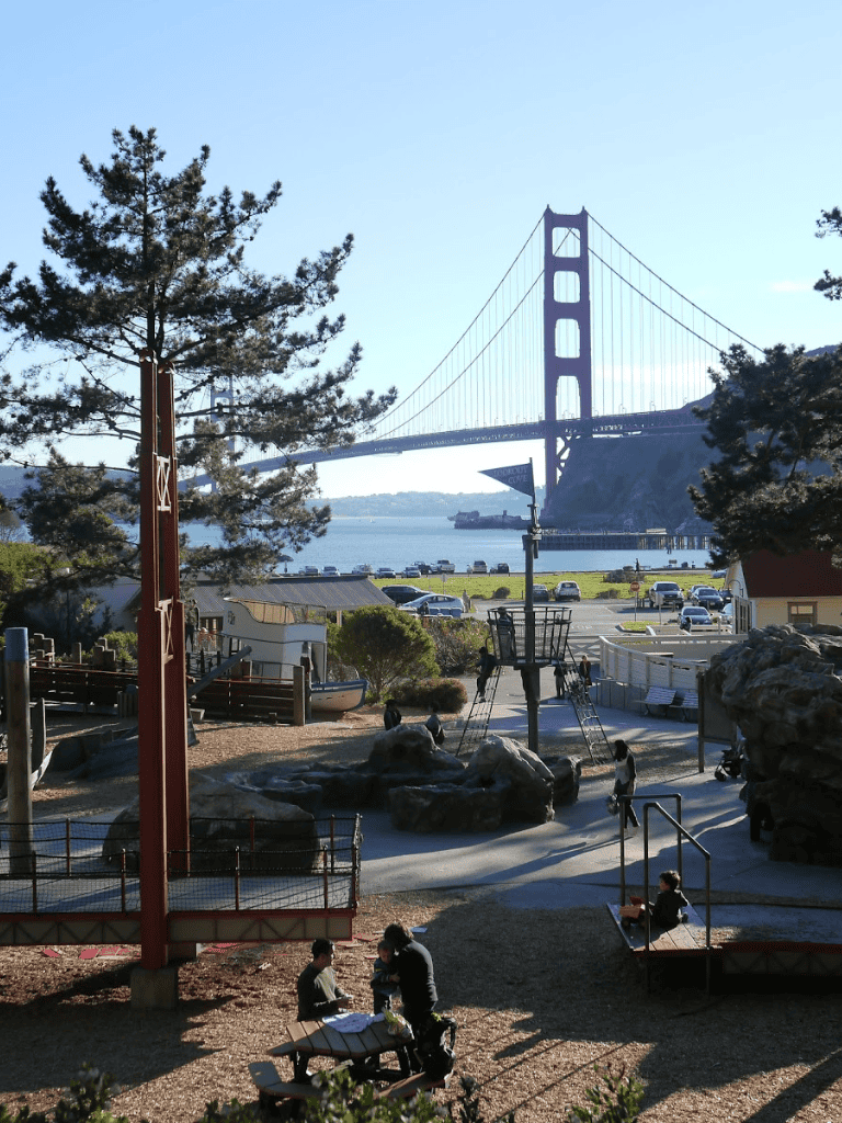 Golden Gate Bridge viewed from outdoor park with children playing and scenic waterfront background.