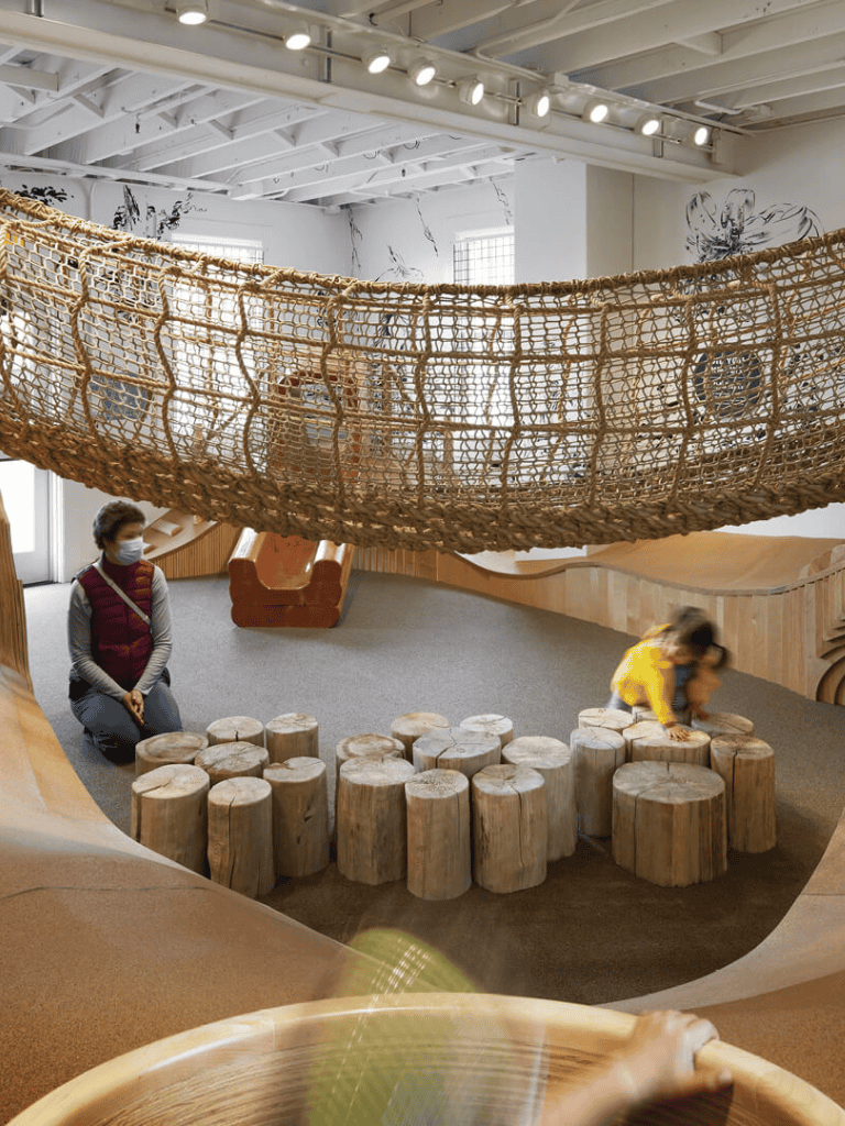 Child-friendly indoor play area with wooden logs and climbing structures for kids’ entertainment.