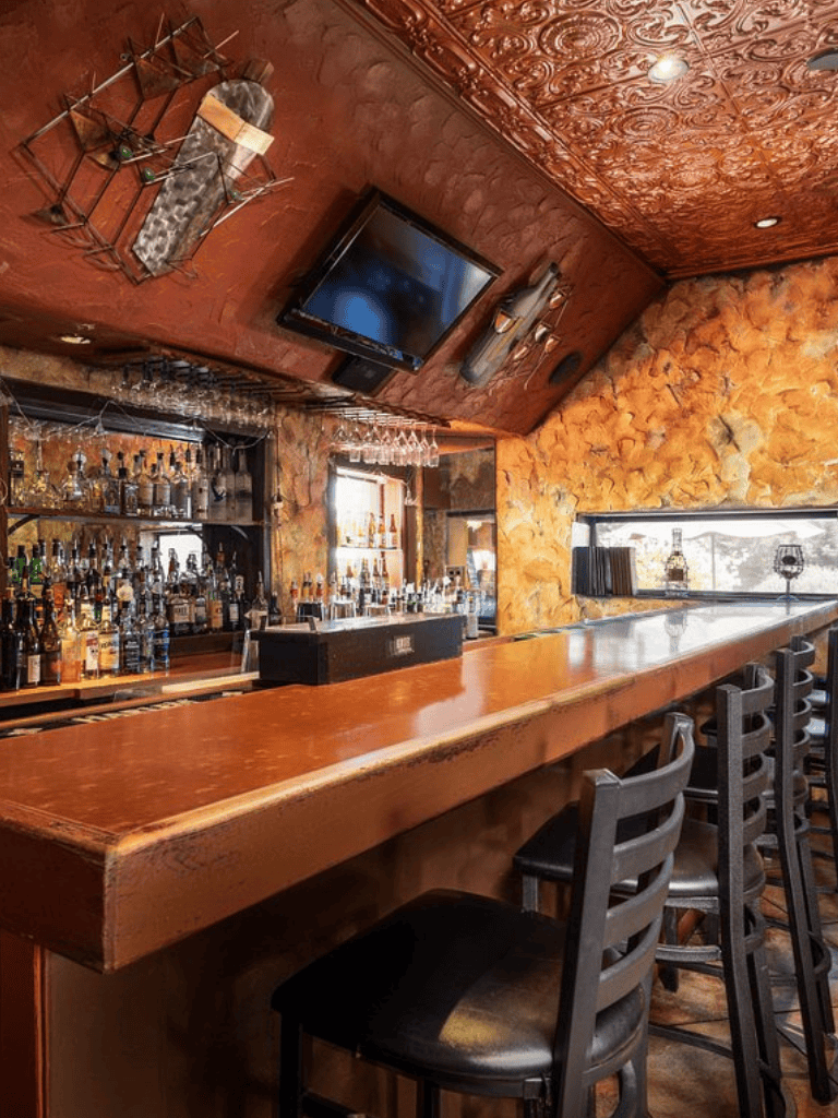 Warm wood bar with liquor bottles, wall-mounted TV, cozy rustic interior, and barstools at QuestForDirections.
