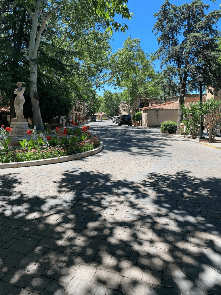 Serene tree-lined street with classical statues and charming architecture, perfect for peaceful neighborhood walks.