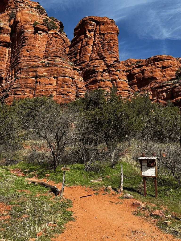 Vivid red rock formations in a desert landscape with trail path and informational sign.