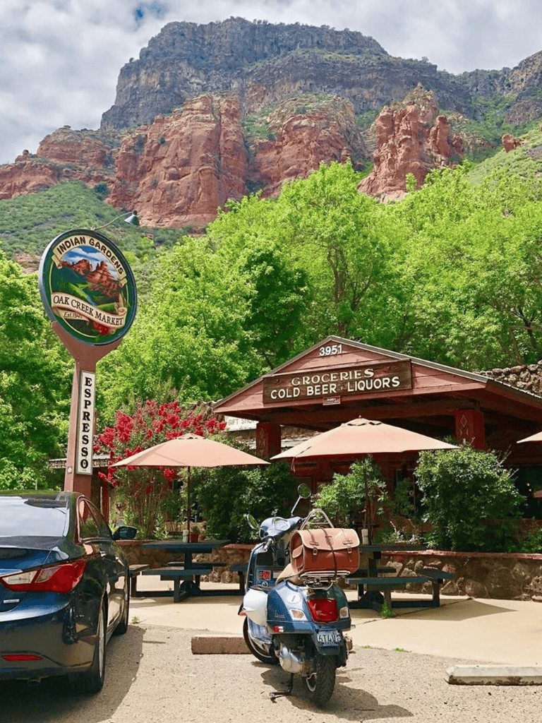 Colorful mountain scene with Indian Gardens market, outdoor seating, and scooter in Oak Creek, Sedona, AZ.
