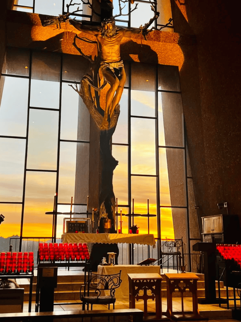 Modern church interior with large crucifix sculpture during sunset light.