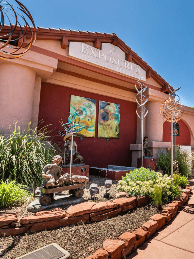 Colorful art gallery entrance with metal sculptures and lush greenery, showcasing fine art displays at Exposures Gallery of Fine Art.