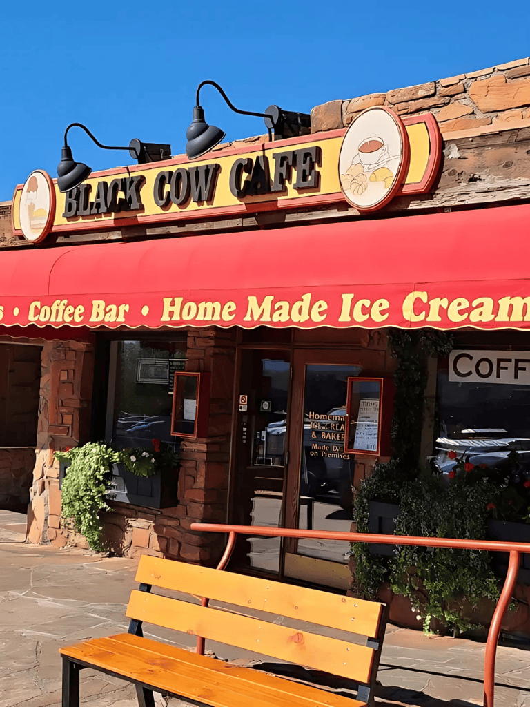Coffee shop with "Black Cow Cafe" sign and outdoor seating, offering coffee, ice cream, and baked goods.