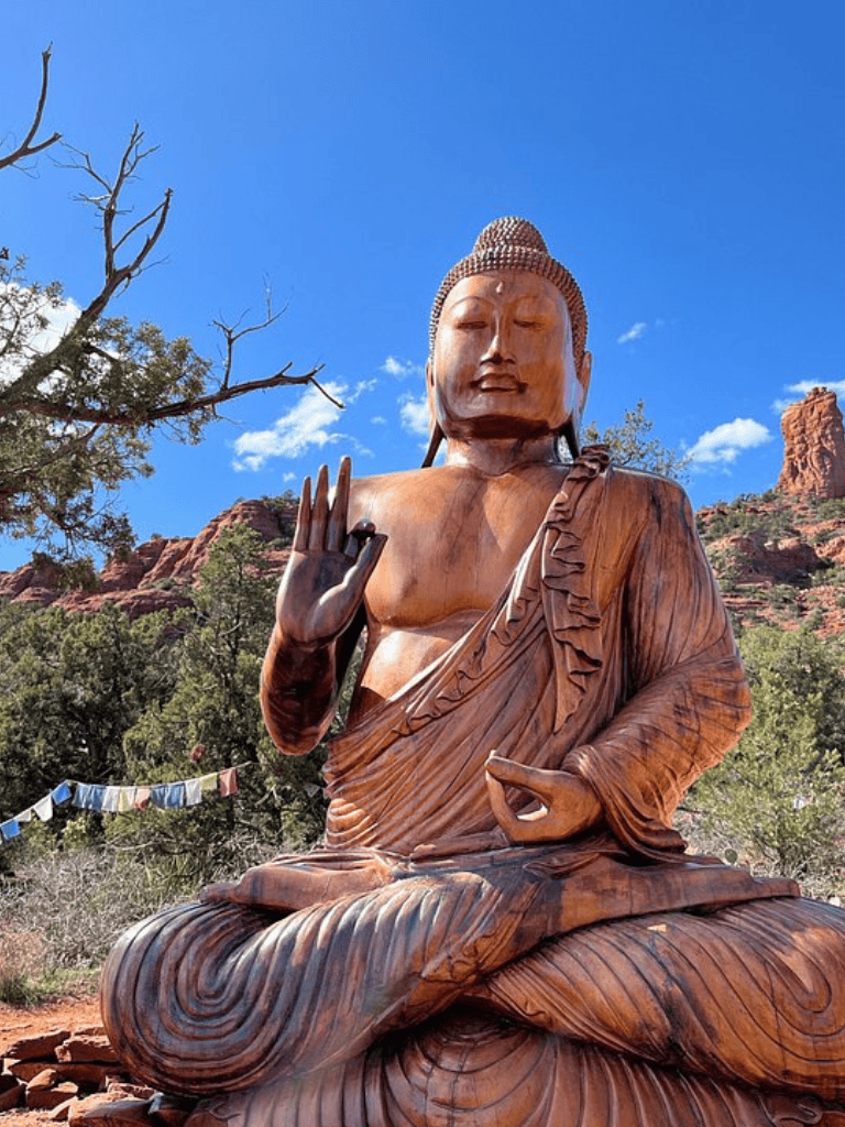 Wooden Buddha statue in outdoor desert landscape under clear blue sky.