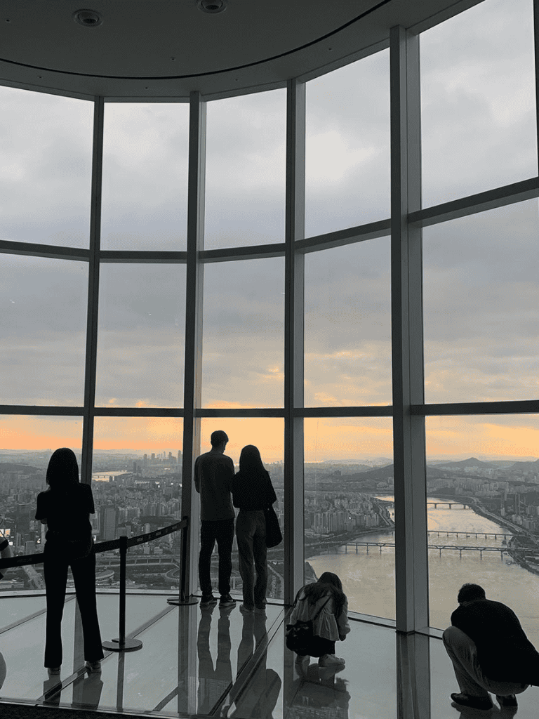Panoramic city view from observation deck at sunset, visitors enjoying high-rise skyline scenery.