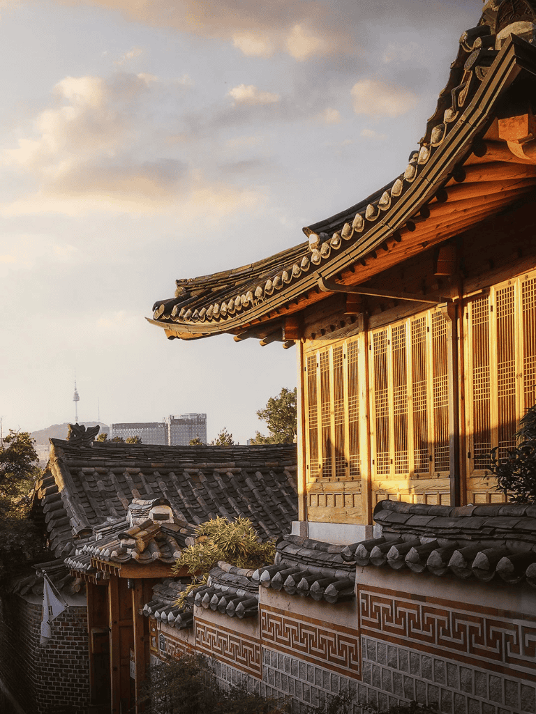 Traditional Korean house with ornate tiled roof and wooden lattice windows at sunset.