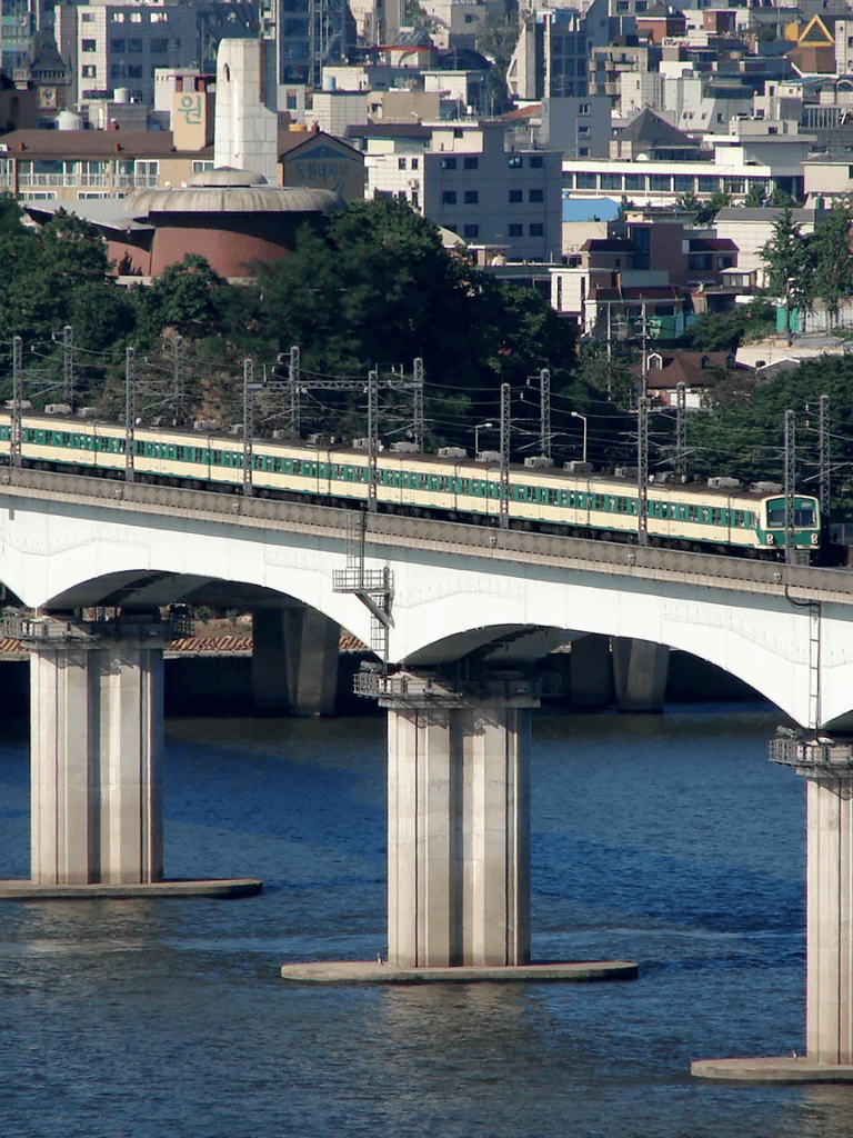 Modern train crossing cityscape in Seoul, South Korea| Urban transportation bridge and train system| A scenic view of Seoul's railway infrastructure showcasing urban transit excellence.