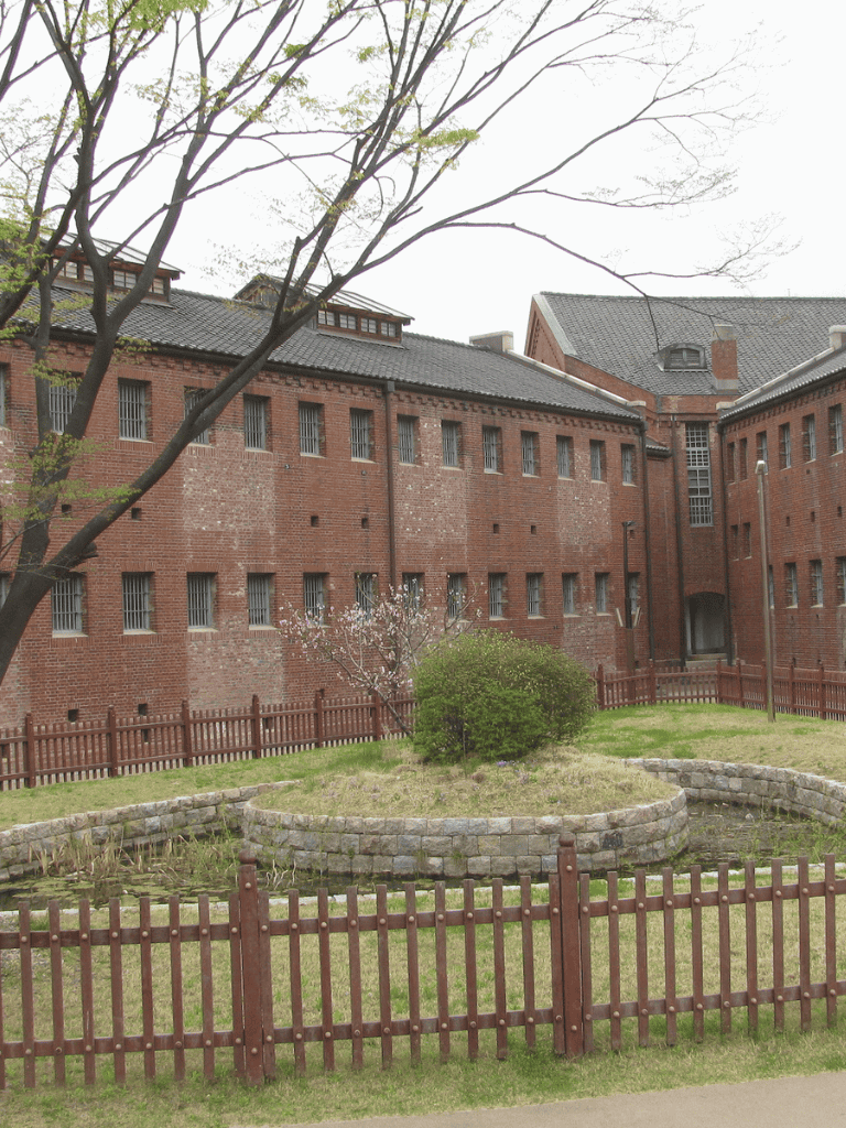 Red brick building with small windows and surrounding greenery, historic architecture, QuestForDirections.