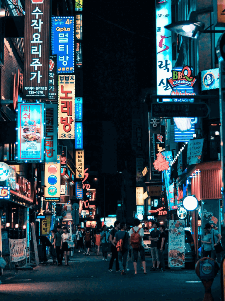 Bright neon signs illuminate a bustling city street in Seoul at night.