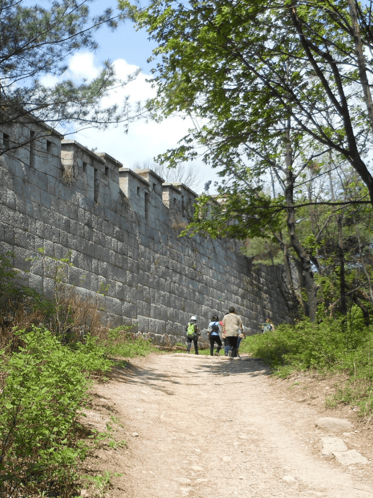Ancient wall along a hiking trail with hikers exploring outdoors in a historic site.