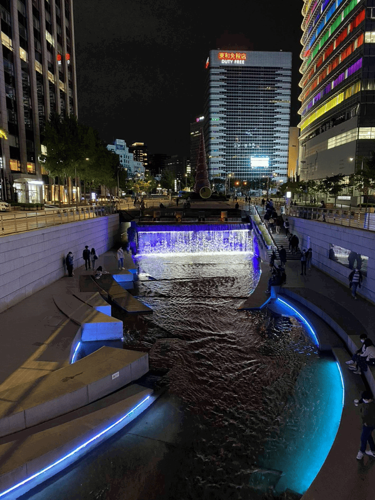 Water fountain with colorful lighting in a modern urban cityscape at night.