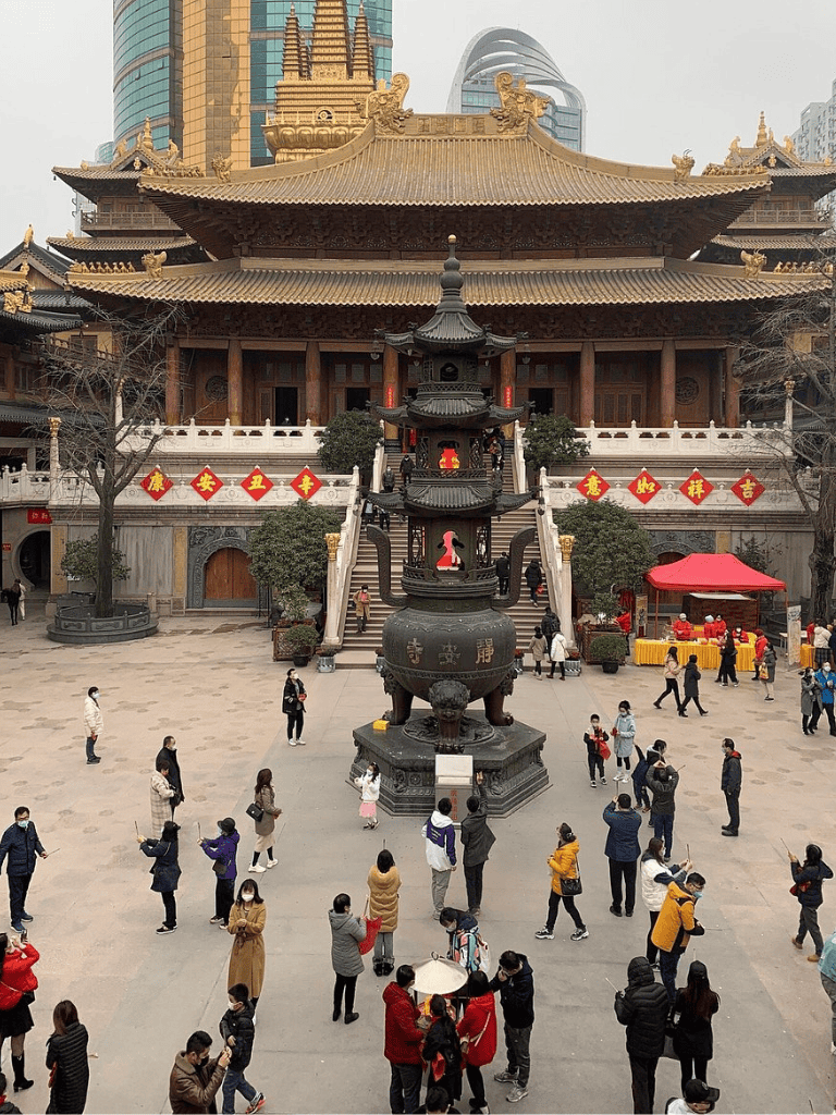 Ancient Chinese temple with visitors, traditional architecture, and modern city skyline background.