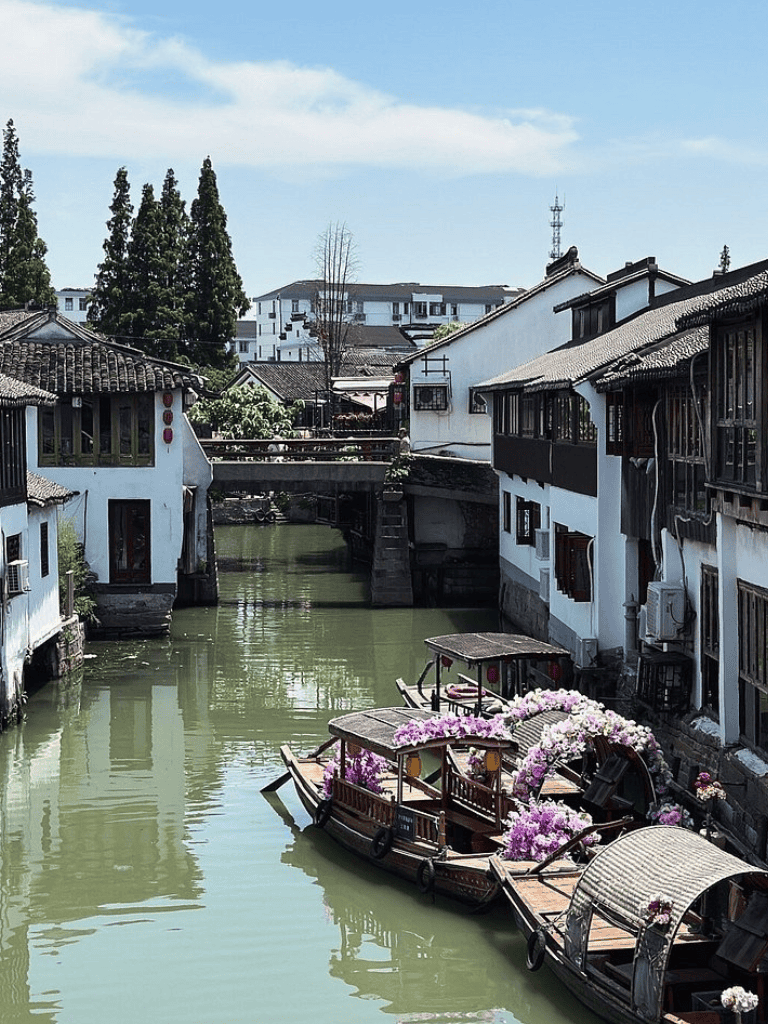 Tranquil water town with traditional Chinese architecture and decorated boats along canal.