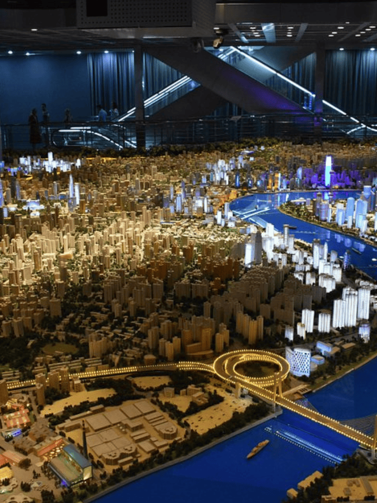 Vibrant cityscape model of a modern urban development with illuminated skyscrapers and a river.