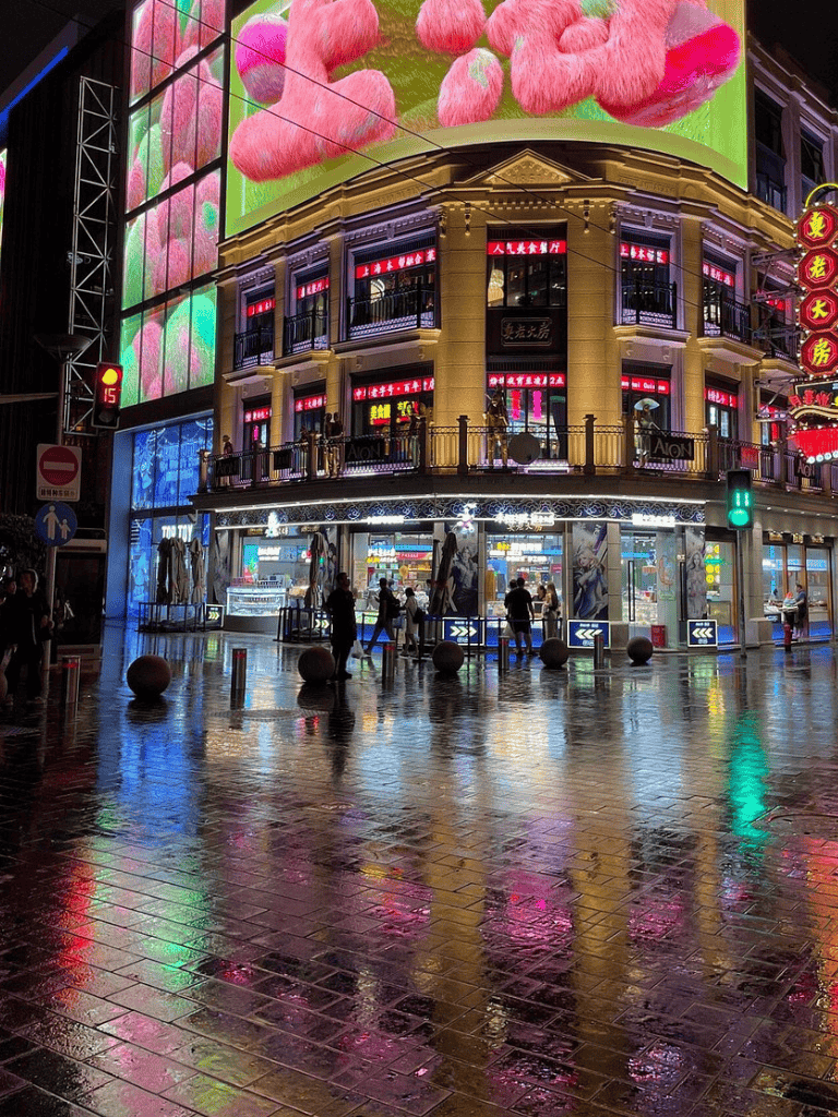 Colorful neon-lit storefronts and vibrant digital billboards in a bustling urban area at night.