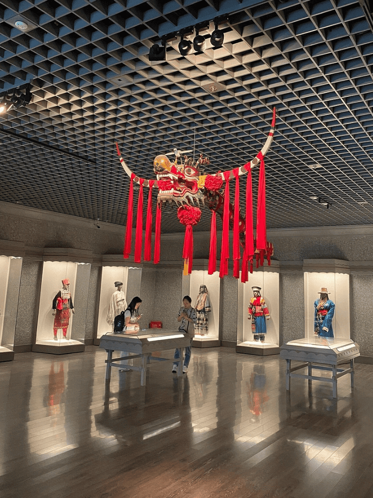 Colorful dragon lantern and traditional costumes in museum exhibit showcasing Asian culture and heritage.