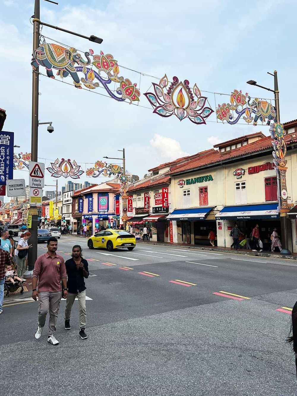 Colorful street decorations in Little India, Singapore with shops, pedestrians, and a yellow car.