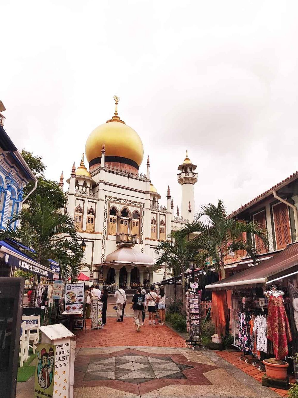 Intricate mosque with golden domes and minarets in a bustling marketplace setting.