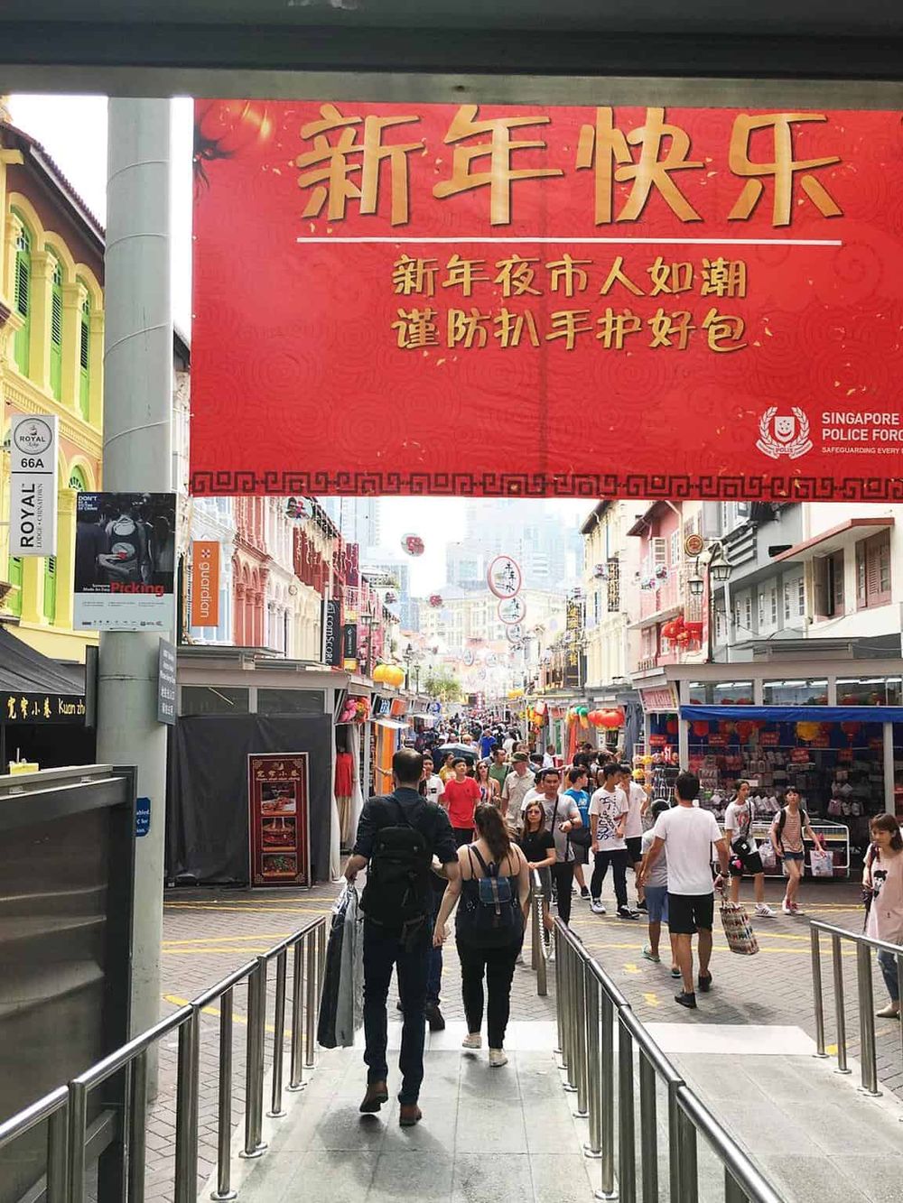Colorful street market in Singapore with festive decorations and crowded shoppers, celebrating Chinese New Year.