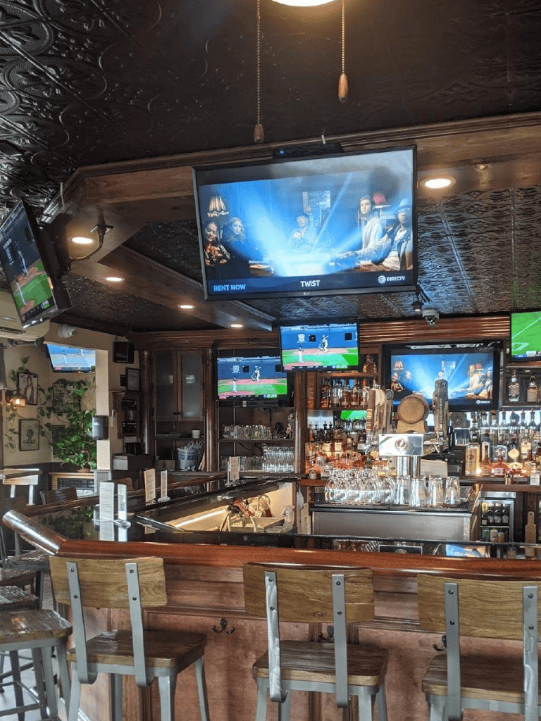 Cozy bar with multiple TV screens, wooden décor, and a welcoming atmosphere for sports fans and social gatherings.